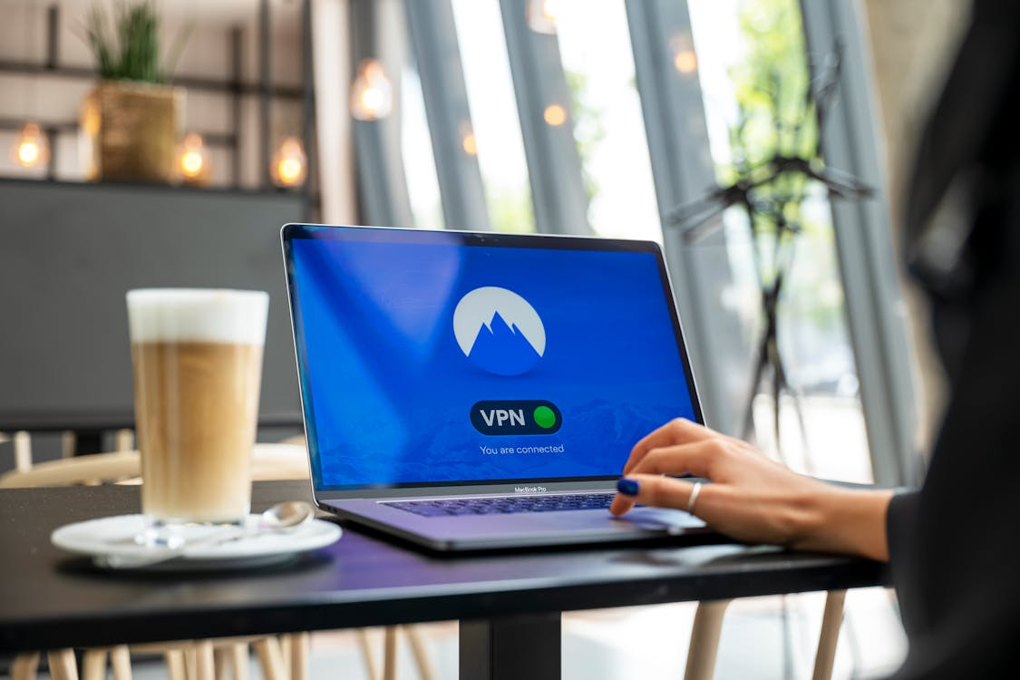 Laptop showing VPN connected screen in a café with a person using public Wi-Fi for secure browsing